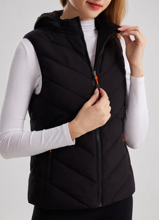 Female model zipping black hooded heated vest, chevron quilting design, orange zipper pull, sleeveless thermal gilet, studio close-up shot, ladies winter heated vest.